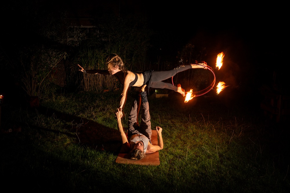 AcroYoga side star: a flyer balances sideways on the base's feet with a burning fire hoop at her feet