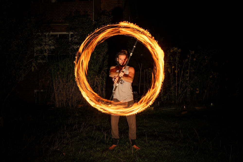 Performer spinning a fire staff so that it draws a glowing circle of flames in the dark
